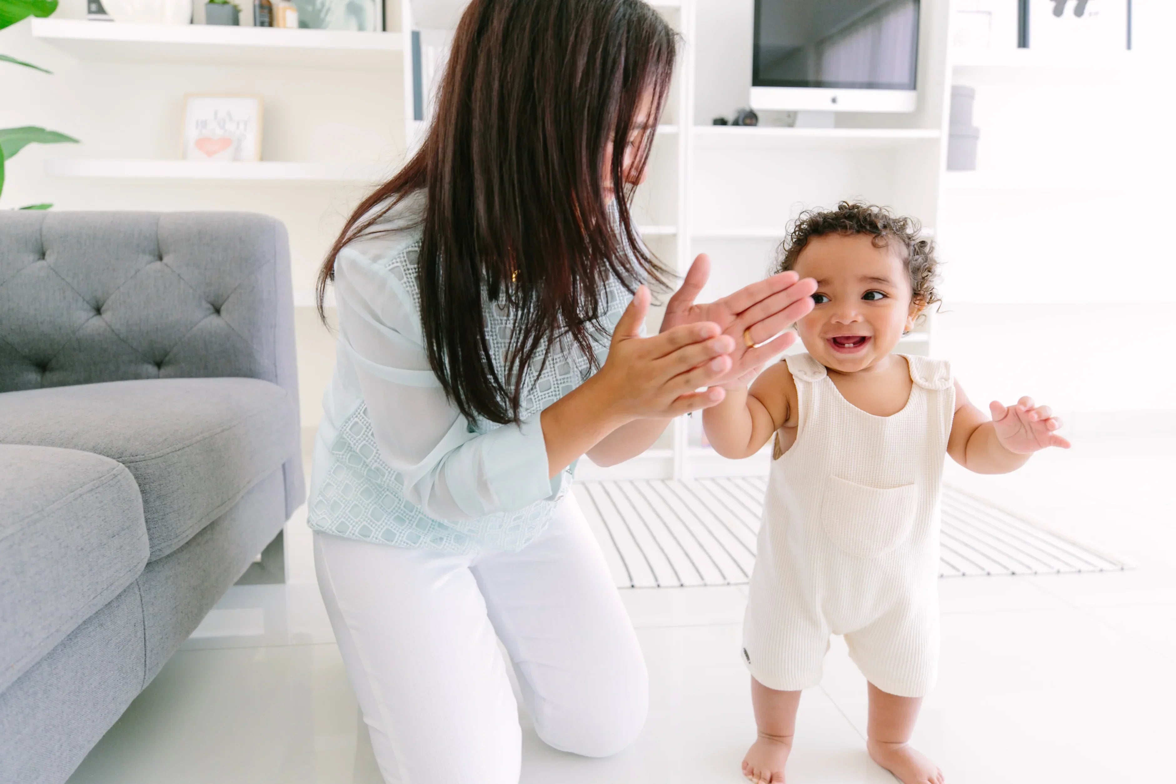 A mother clapping and encouraging her toddler as they dance together, enjoying a joyful and interactive music session.