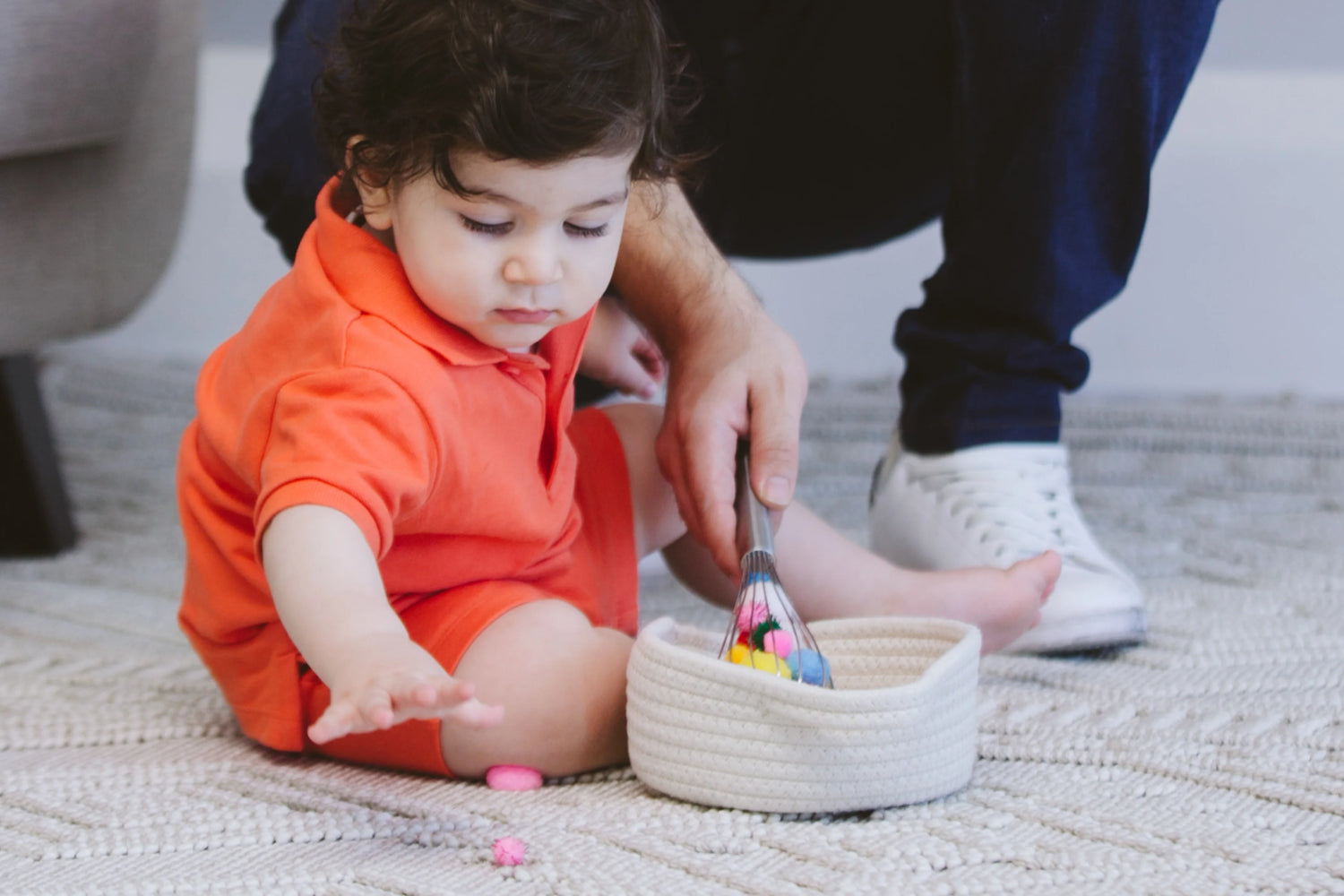 Toddler playing with colorful sticks in a safe container, exploring and developing fine motor skills