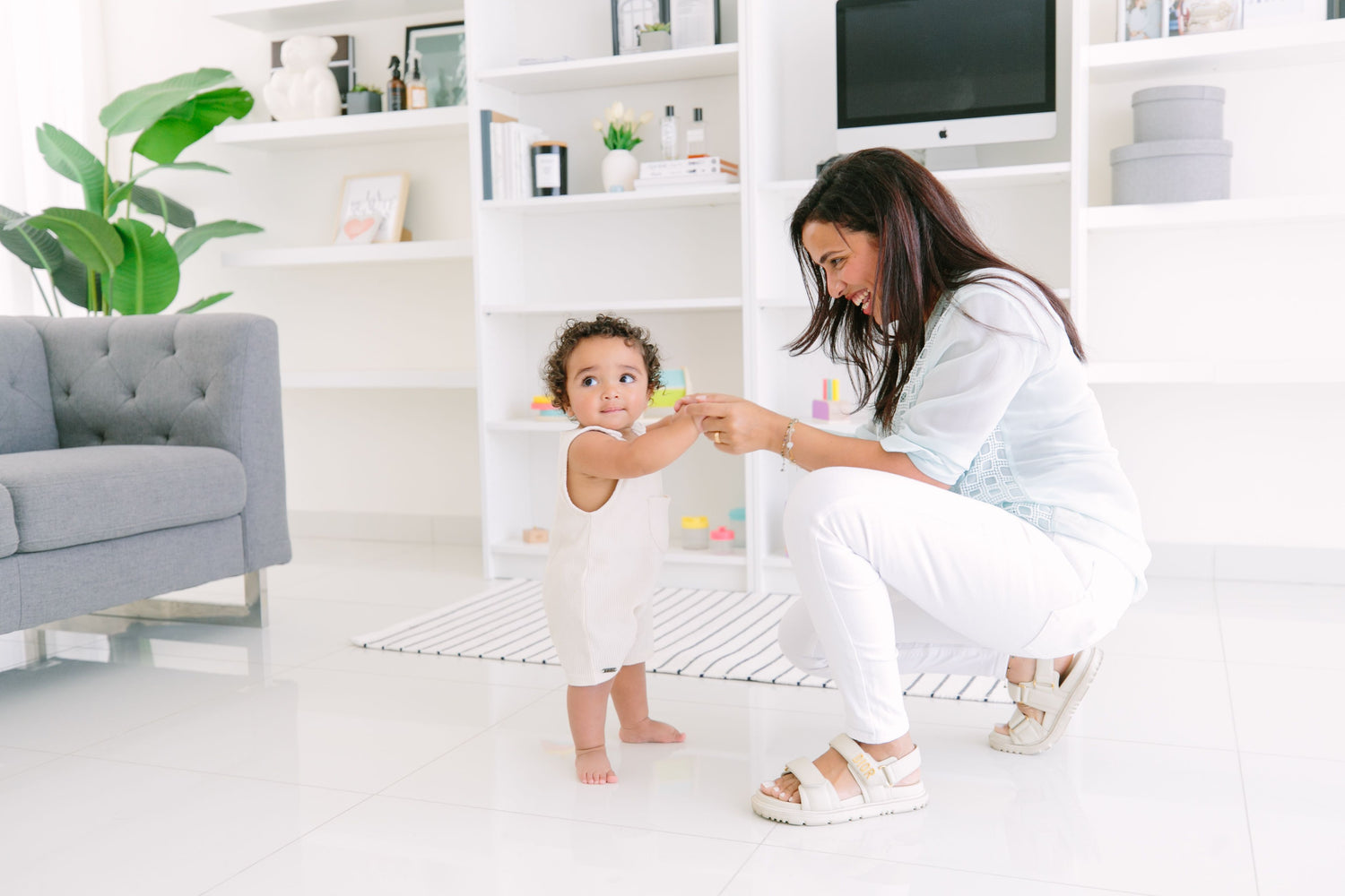 Toddler taking first steps with parental support, developing gross motor skills and learning to walk in a safe, Montessori-inspired environment.