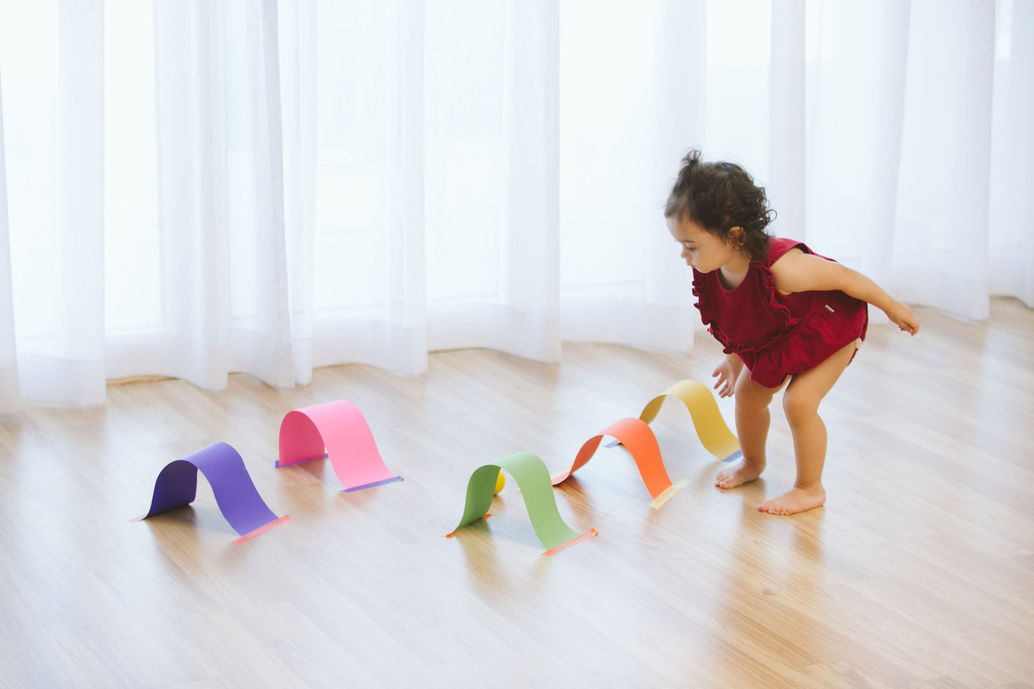 Toddler engaging with colorful paper arches taped to the floor, navigating through them as part of a gross motor skills activity designed to enhance movement and coordination.